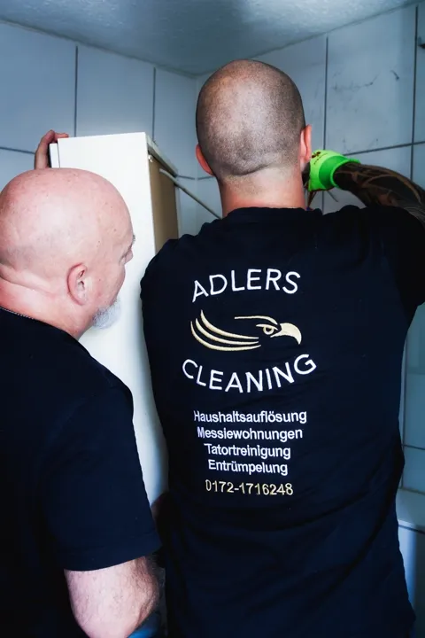 Zwei Mitarbeiter von Adlers Cleaning tragen einen Einbauschrank aus einem Badezimmer